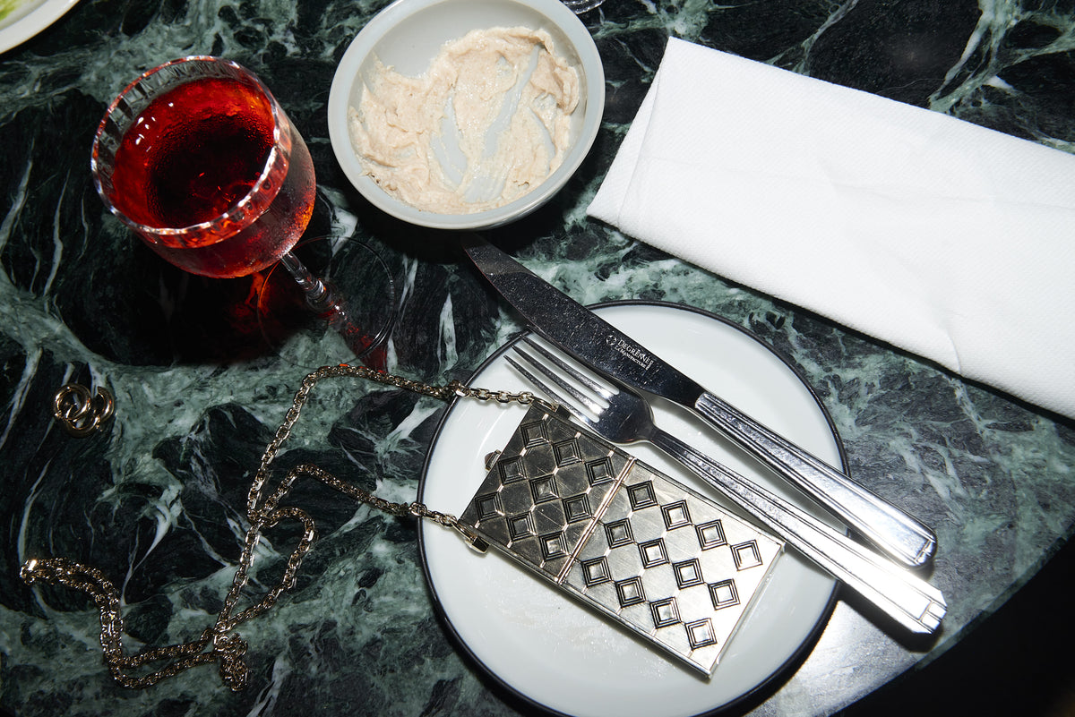 Luxury gold cigarette case necklace by SEDNON on a stylish table, highlighting its design and artisanal craftsmanship in a fashionable setting.